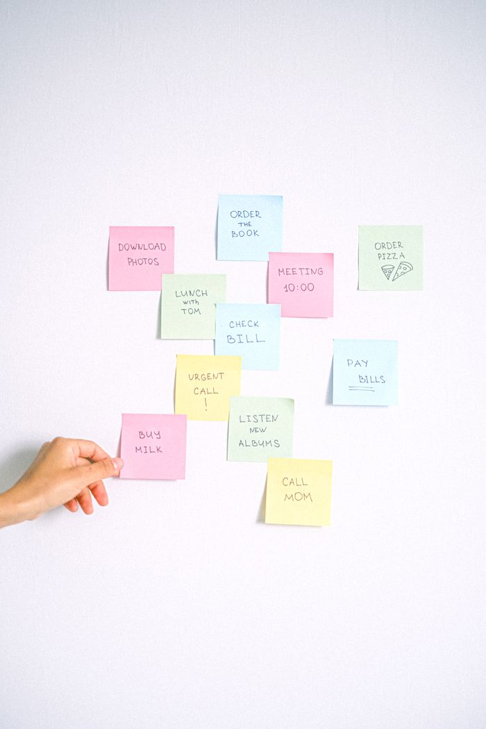 Hand arranging colorful sticky notes with reminders on a white wall.